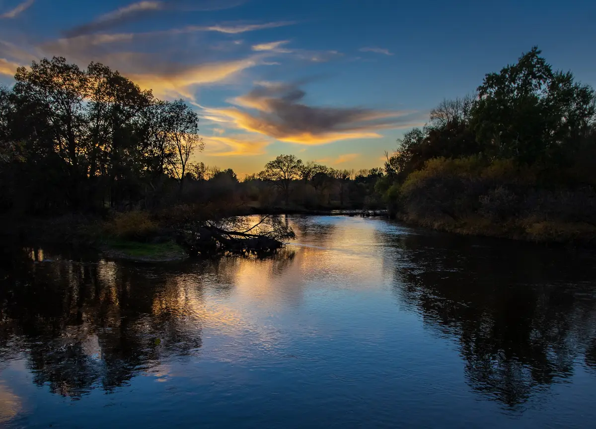 Calm river at sunset with tree-lined banks, where the Pine River joins the Chippewa River at Chippewa Nature Center