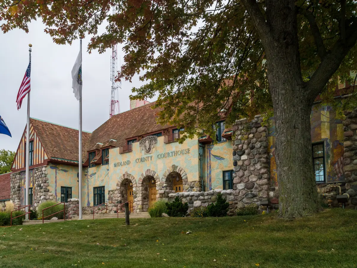 The Midland County Courthouse, a Tudor Revival building with fieldstone arches, painted stucco walls with murals, and flags out front under autumn leaves